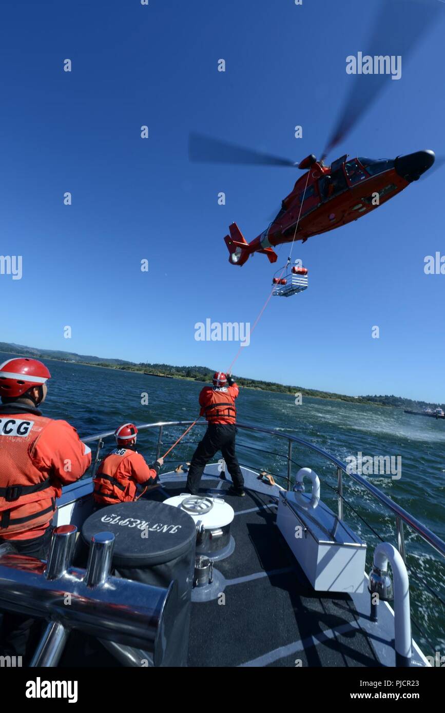 D'équipage à bord des 52 pieds Bateau de vie intrépide de la Garde côtière de Coos Bay conduite nacelle de sauvetage palan training avec un hélicoptère MH-65 de l'équipe de Dolphin Secteur North Bend, Oregon, le 19 juillet 2018. La Garde côtière procède à la formation comme ce palan panier sur une base régulière afin de maintenir les membres de service préparé pour une éventuelle évacuation de l'air en mer. Banque D'Images