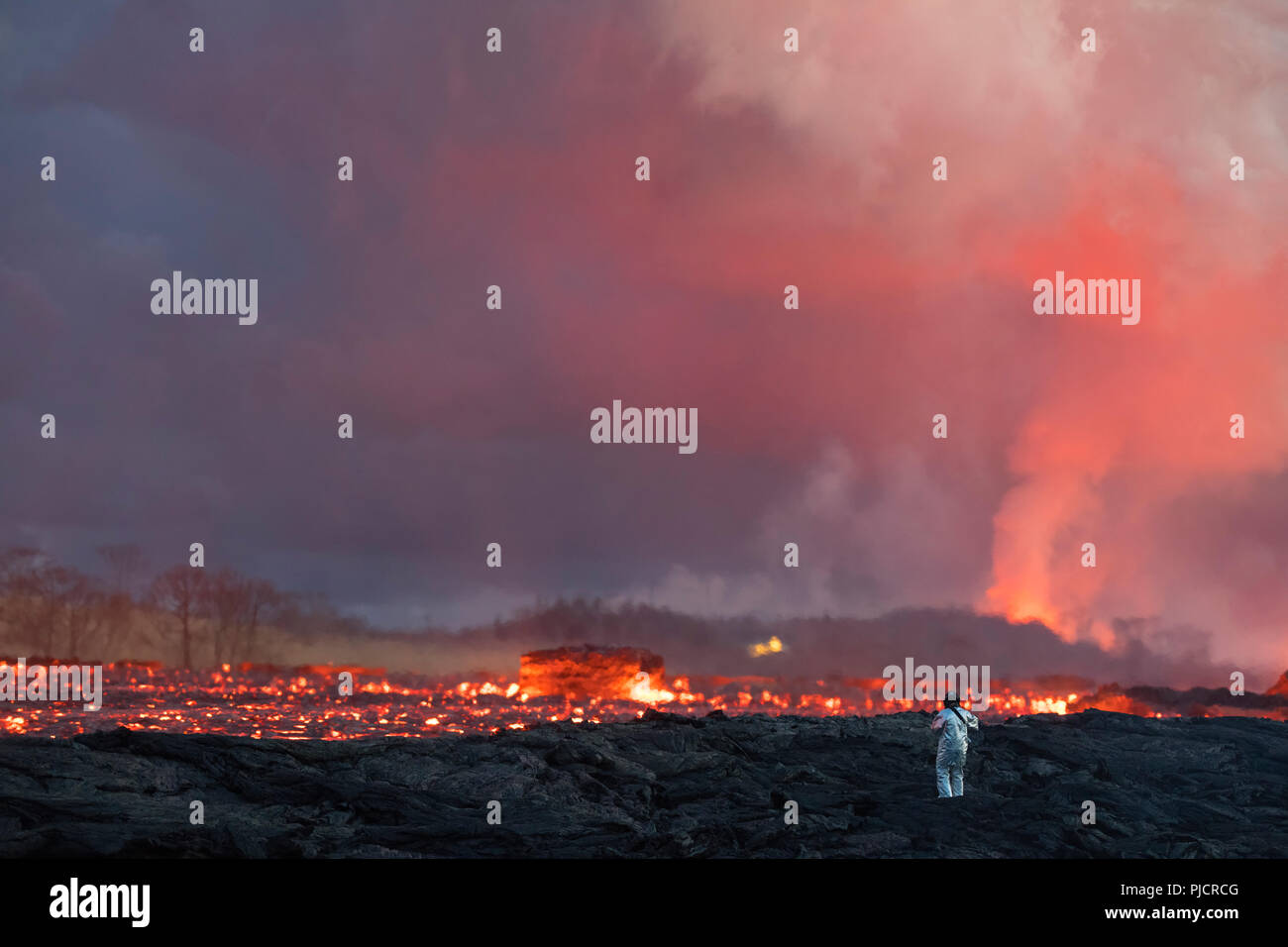 Un équipement de protection thermique tests des pompiers à côté d'un fleuve de lave bouillante éruption de 8 fissure (en arrière-plan) de l'est zone de rift volcan Kilauea Banque D'Images