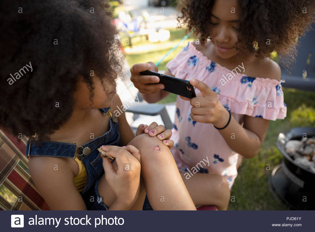 Fille avec téléphone appareil photo photographier avec soeur genou écorché Banque D'Images
