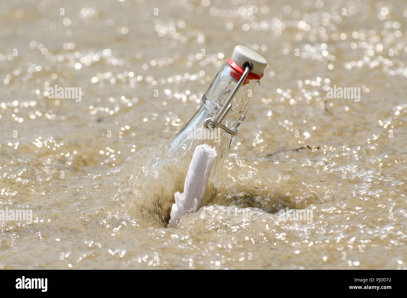 Message dans une bouteille couchée dans le sable sur la plage avec de l'eau. Banque D'Images