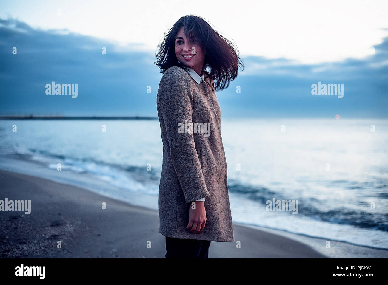 Portrait of young woman standing on beach, looking over Shoulder, smiling Banque D'Images