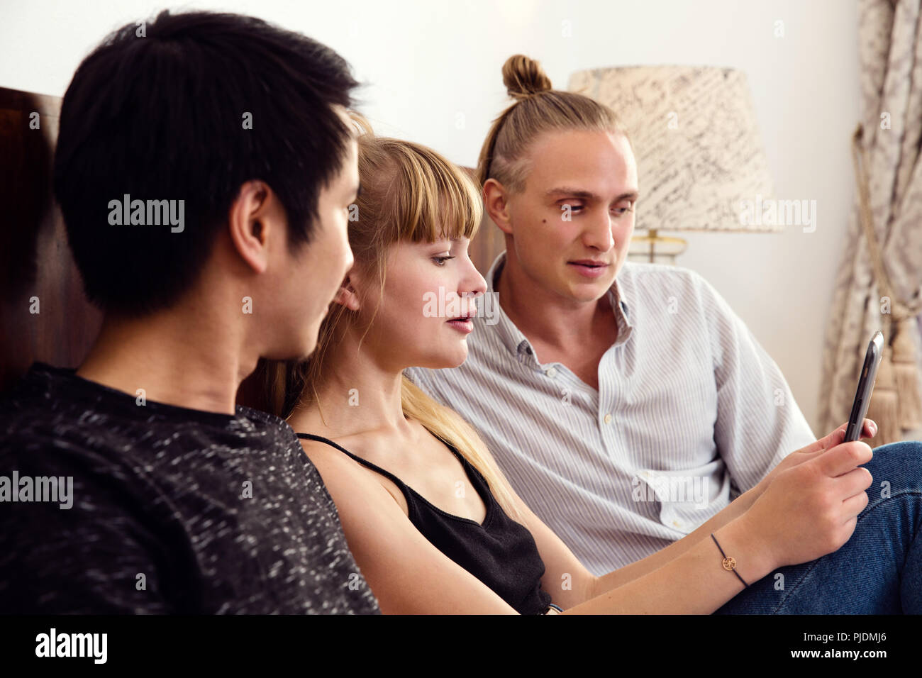 Jeune femme et homme amis looking at smartphone on bed Banque D'Images