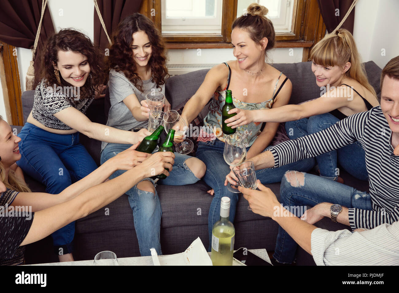 Groupe d'amis adultes hommes et femmes assis sur canapé faire un toast Banque D'Images