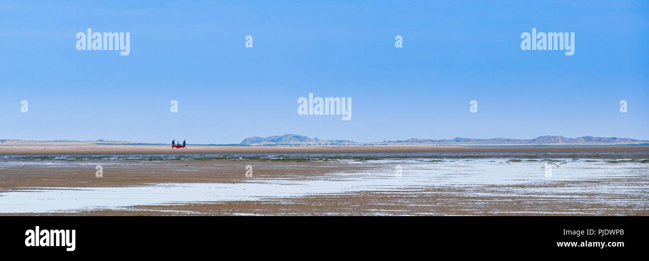 Un petit group de gens marcher à travers une plage vide. Banque D'Images