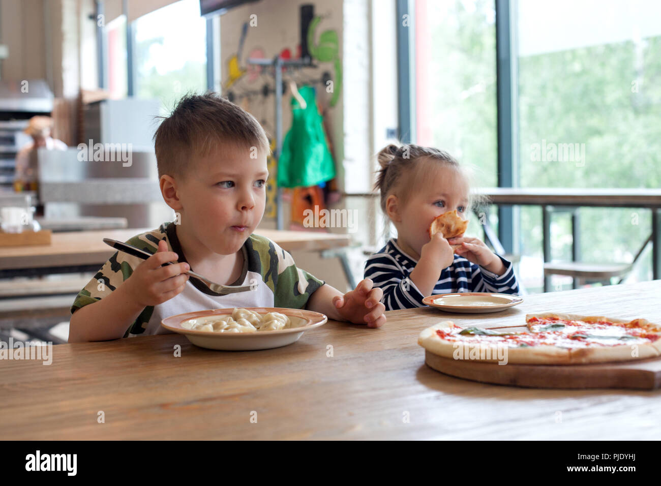 Les enfants peuvent manger des pizzas et de beignets de viande cafe. Les enfants de manger des aliments malsains à l'intérieur. Frères et sœurs dans le café, des vacances en famille concept. Banque D'Images