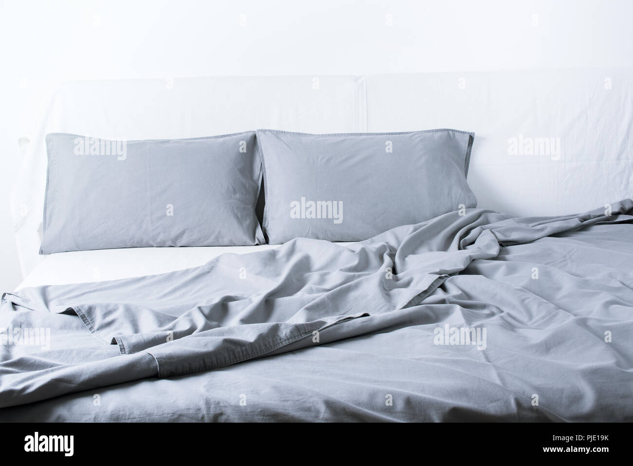 Close Up Literie Linge gris couvre-lit oreiller Fiche Mur Blanc Arrière-plan de la salle intérieur concept lit malpropre Banque D'Images