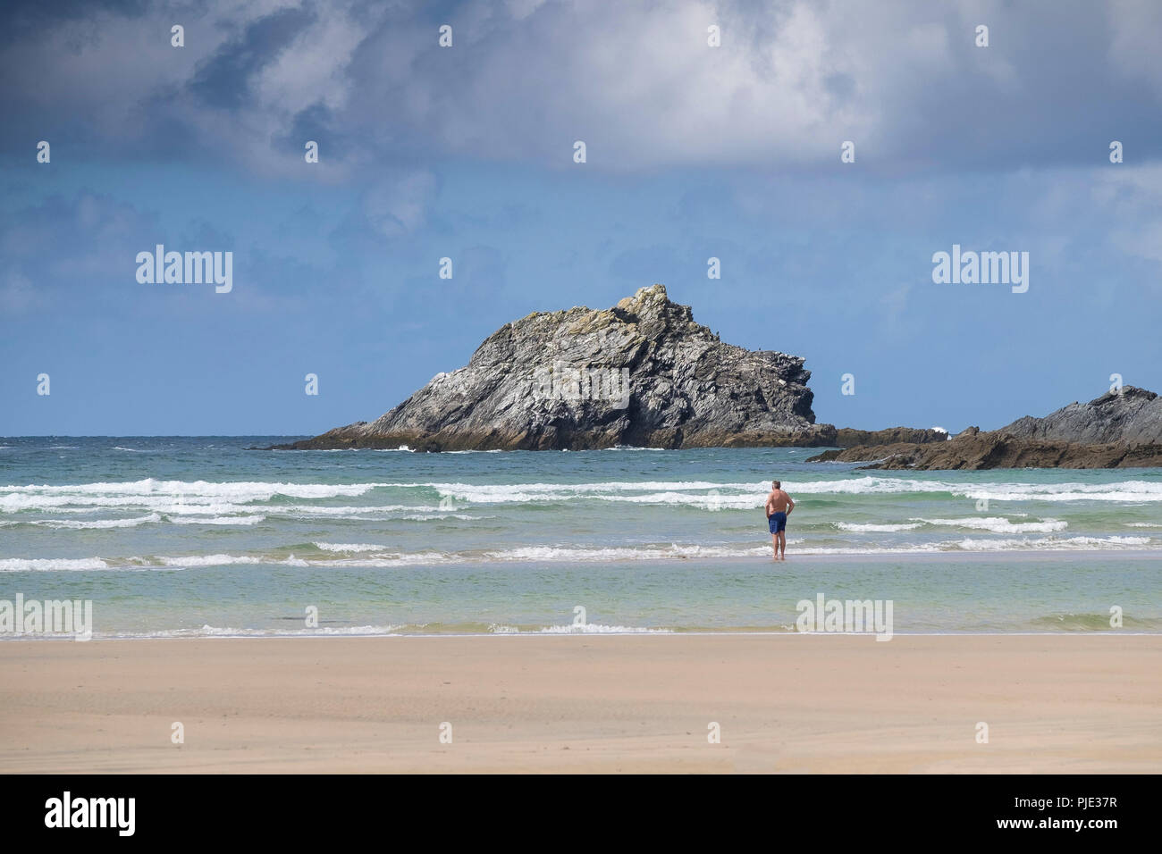 Le voyageur debout dans la mer à Crantock Beach à la recherche sur l'OIE une petite île inhabitée de rochers au large de Pointe pentire à Newquay Co Banque D'Images
