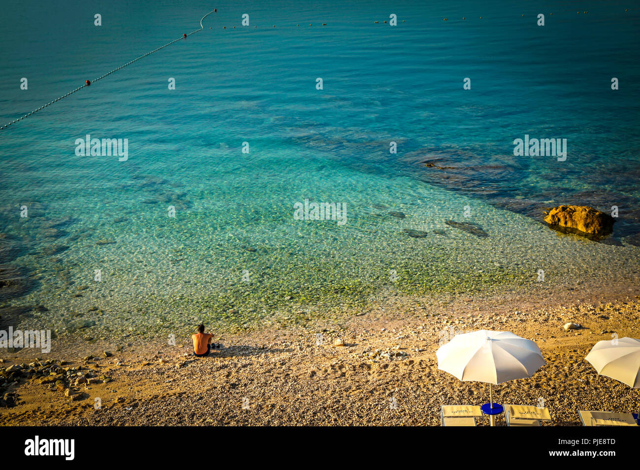 L'homme est assis dans le silence et le calme à l'aube au bord de l'eau de la mer Adriatique au village de Baska, sur l'île croate de Krk Banque D'Images