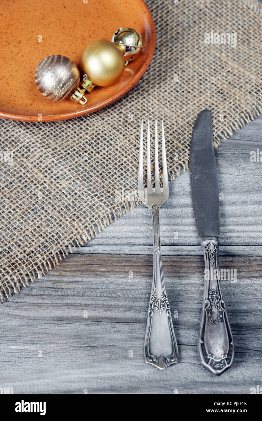 Fourchette et couteau en acier et des boules de Noël sur une plaque en céramique sont situés sur la table en bois, recouvert de tapis grossier Banque D'Images