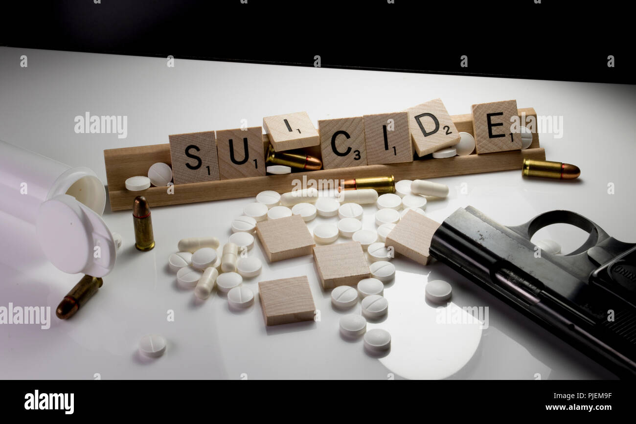 La sensibilisation au suicide Concept écrit avec des lettres de Scrabble avec une arme à la main, bouteille de pilules, des balles et des médicaments renversé sur un tableau blanc. Banque D'Images