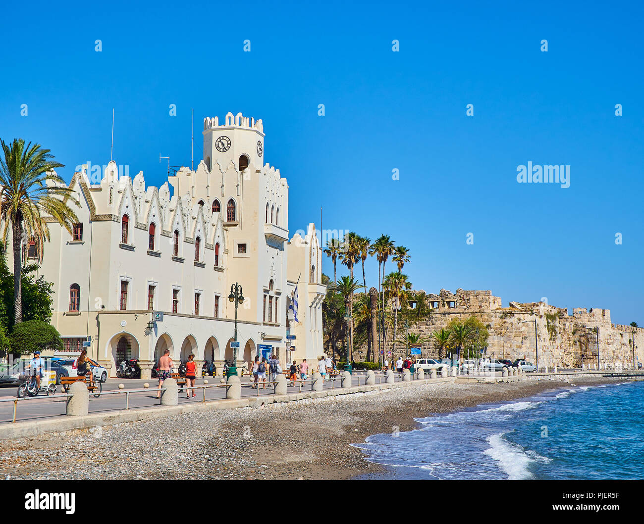 Kos, Grèce - Juillet 3, 2018. Les personnes qui traversent la rue Akti Miaouli avec le Palais du Gouvernement en arrière-plan. L'île grecque de Kos. Région de l'Egée du Sud. Banque D'Images