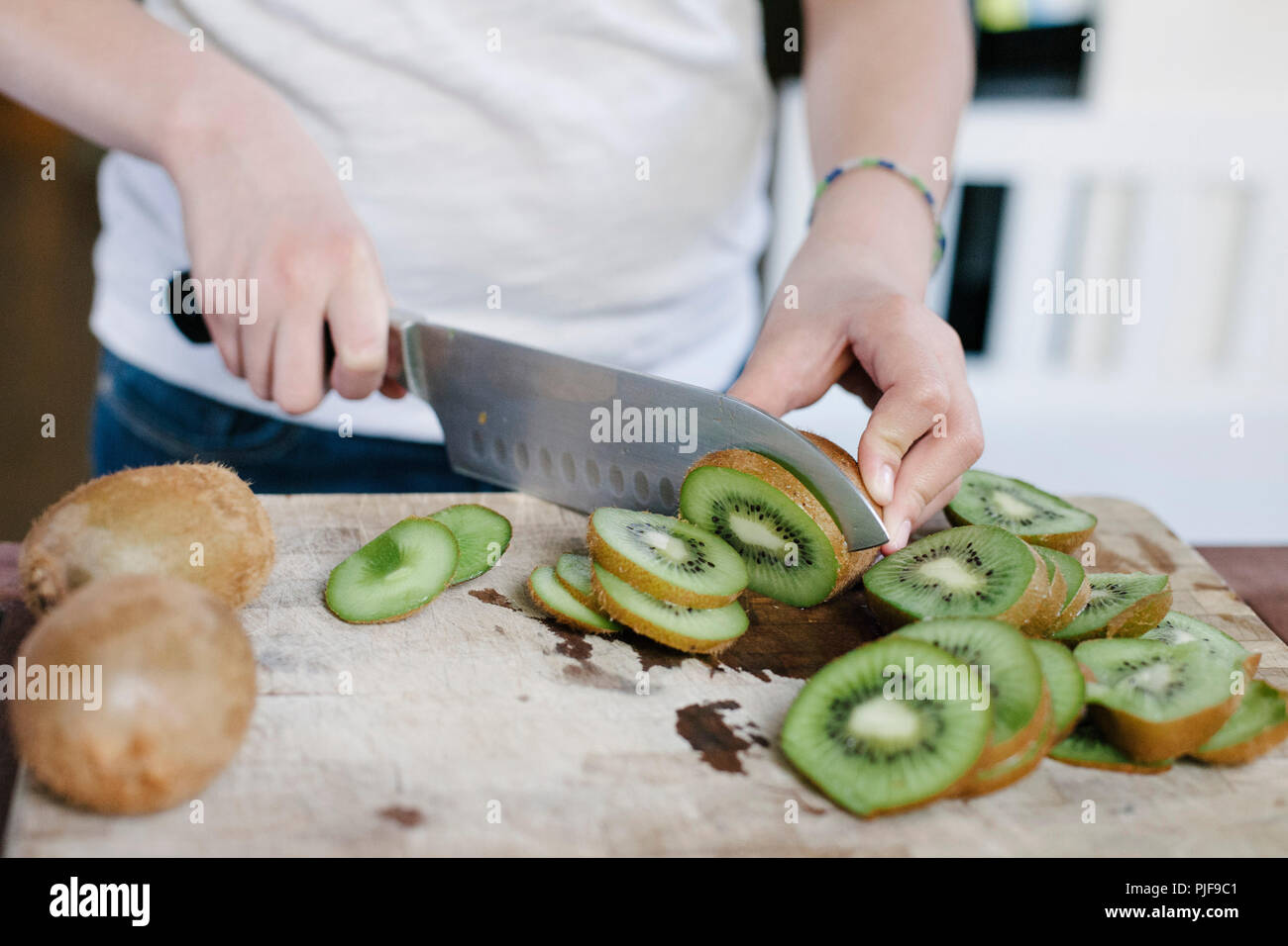 Tranches de kiwi est assis sur une planche à découper avec les mains d'une femme le tranchage Banque D'Images