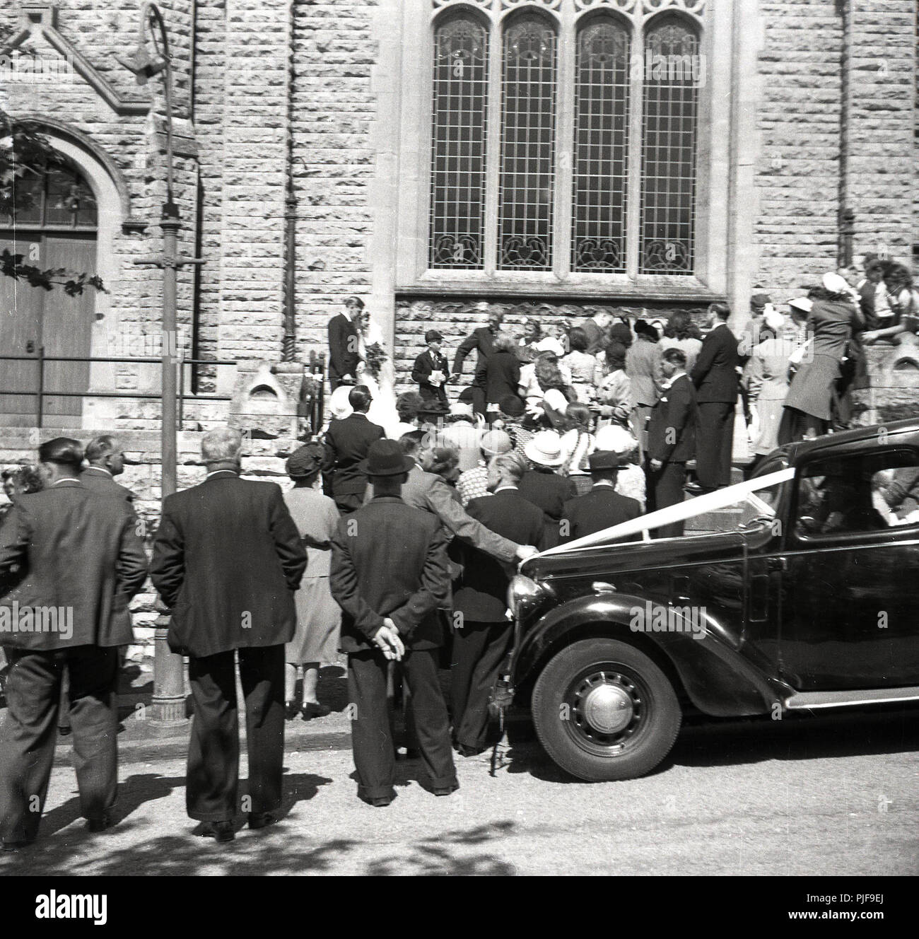 Années 1950, mariage, famille et amis se rassemblent à l'extérieur de l'église pour voir le pont et le marié laissent dans leur voiture de mariage, England, UK. Banque D'Images