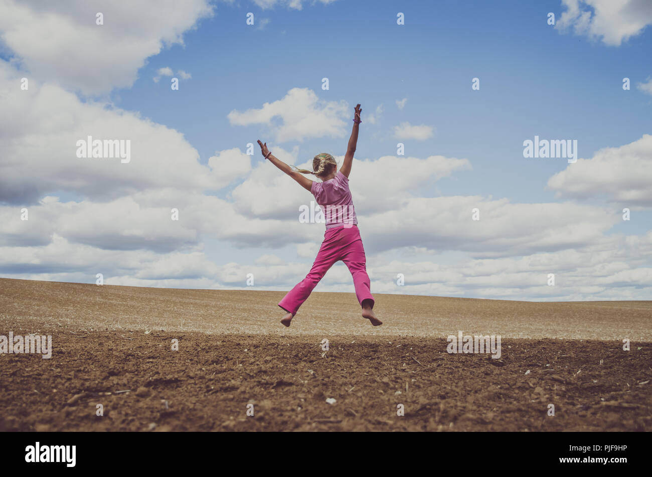 Petite fille sautant seul dans champ labouré dans la campagne pittoresque sous ciel nuageux Banque D'Images