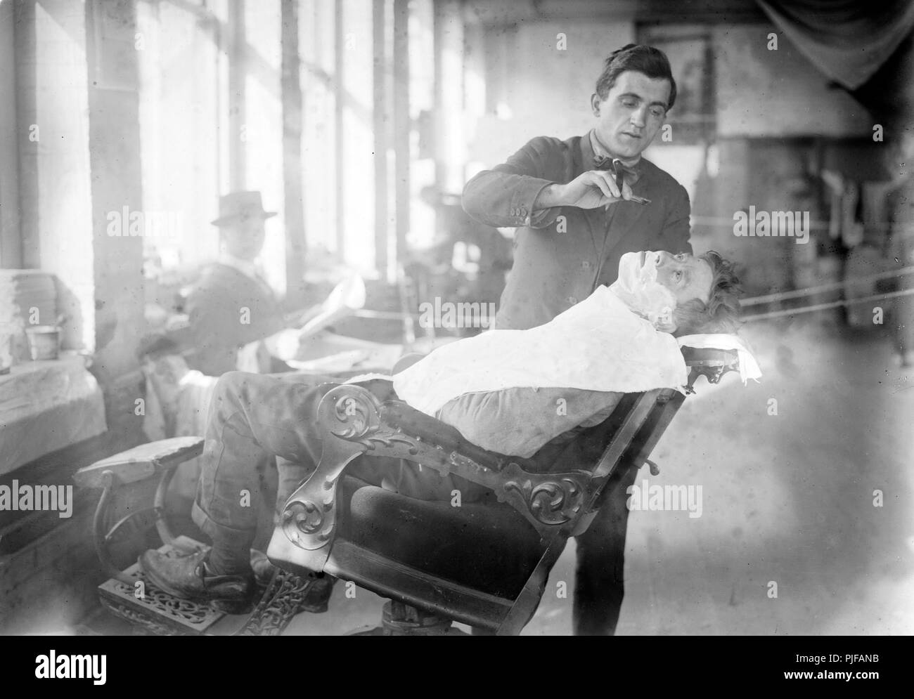 Salon de coiffure, d'une image historique de coiffure donnant un rasage d'un homme, vers 1915 Banque D'Images