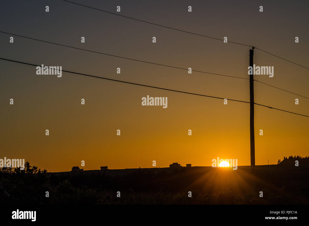 Téléphone et lignes électriques traverser un champ et ciel orange. Coucher du soleil dans la rivière des Français, l'Île du Prince Édouard. Banque D'Images