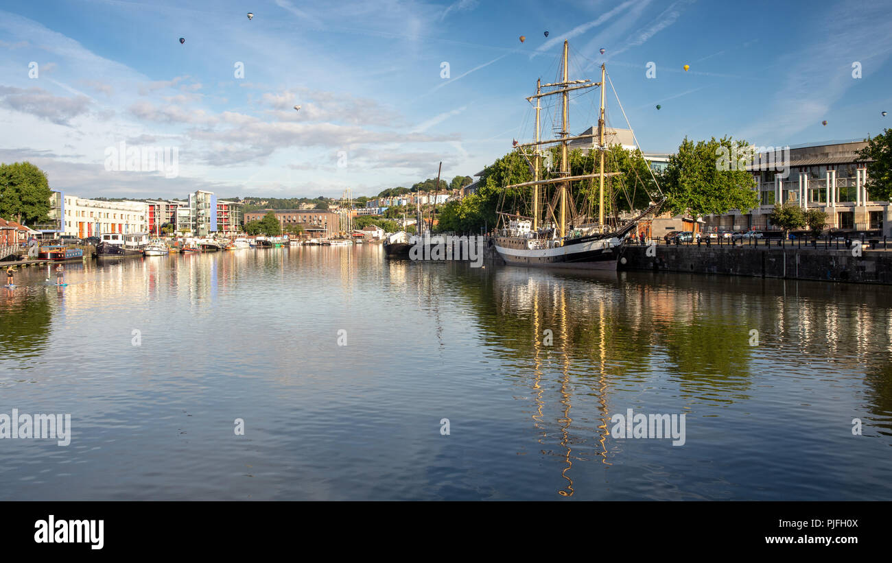 Bristol, Angleterre, Royaume-Uni - 11 août 2018 : montgolfières volent au-dessus d'un grand voilier amarré au port flottant de Bristol à l'aube à l'assemblée annuelle de l'Balloon Banque D'Images