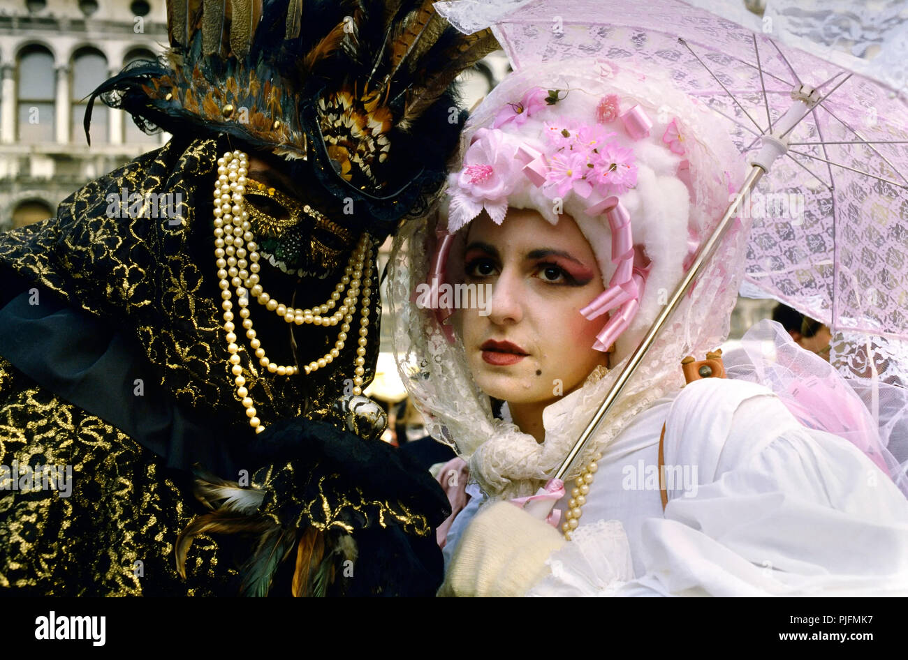 L'Europe, l'Italie, un couple avec masque au Carnaval de Venise. Un homme masqué avec un loup d'or et de perle. Une femme vêtue de blanc vêtu d'un parapluie rose Banque D'Images
