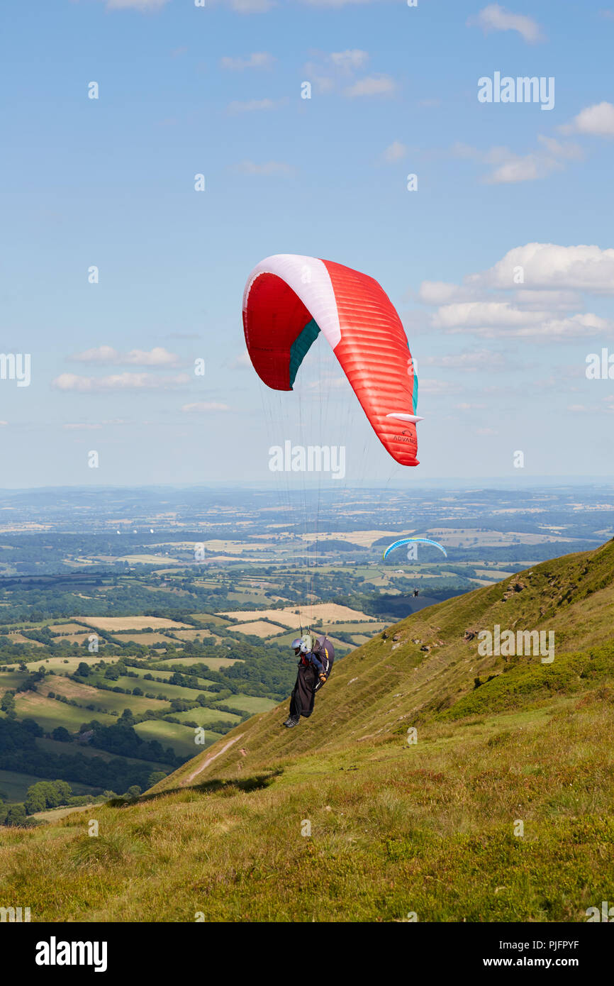 Le dirigeant d'une parapentiste atterrit sur Hay Bluff au-dessus des champs verts au Pays de Galles UK lors d'une journée ensoleillée Banque D'Images