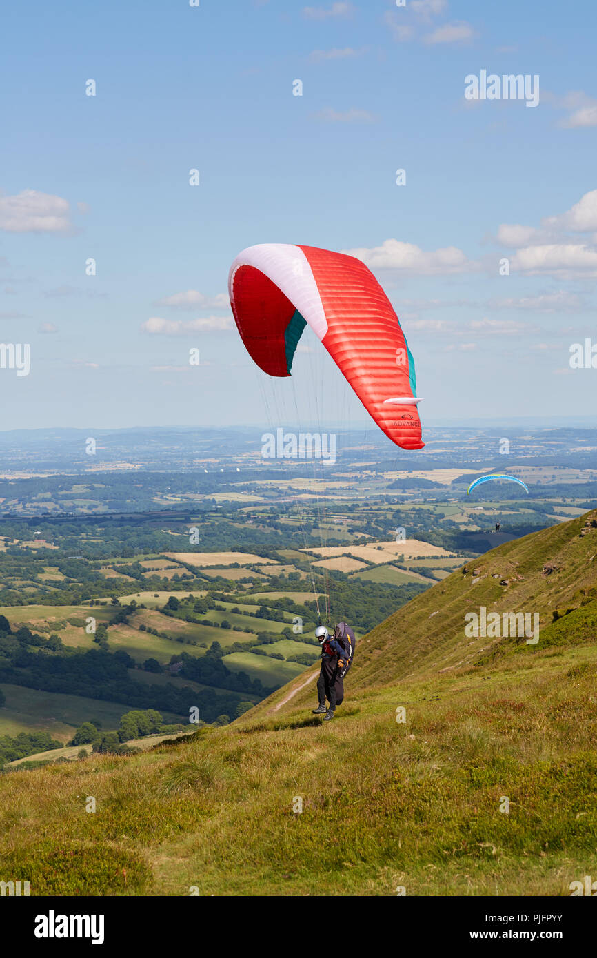 Le dirigeant d'une parapentiste atterrit sur Hay Bluff au-dessus des champs verts au Pays de Galles UK lors d'une journée ensoleillée Banque D'Images