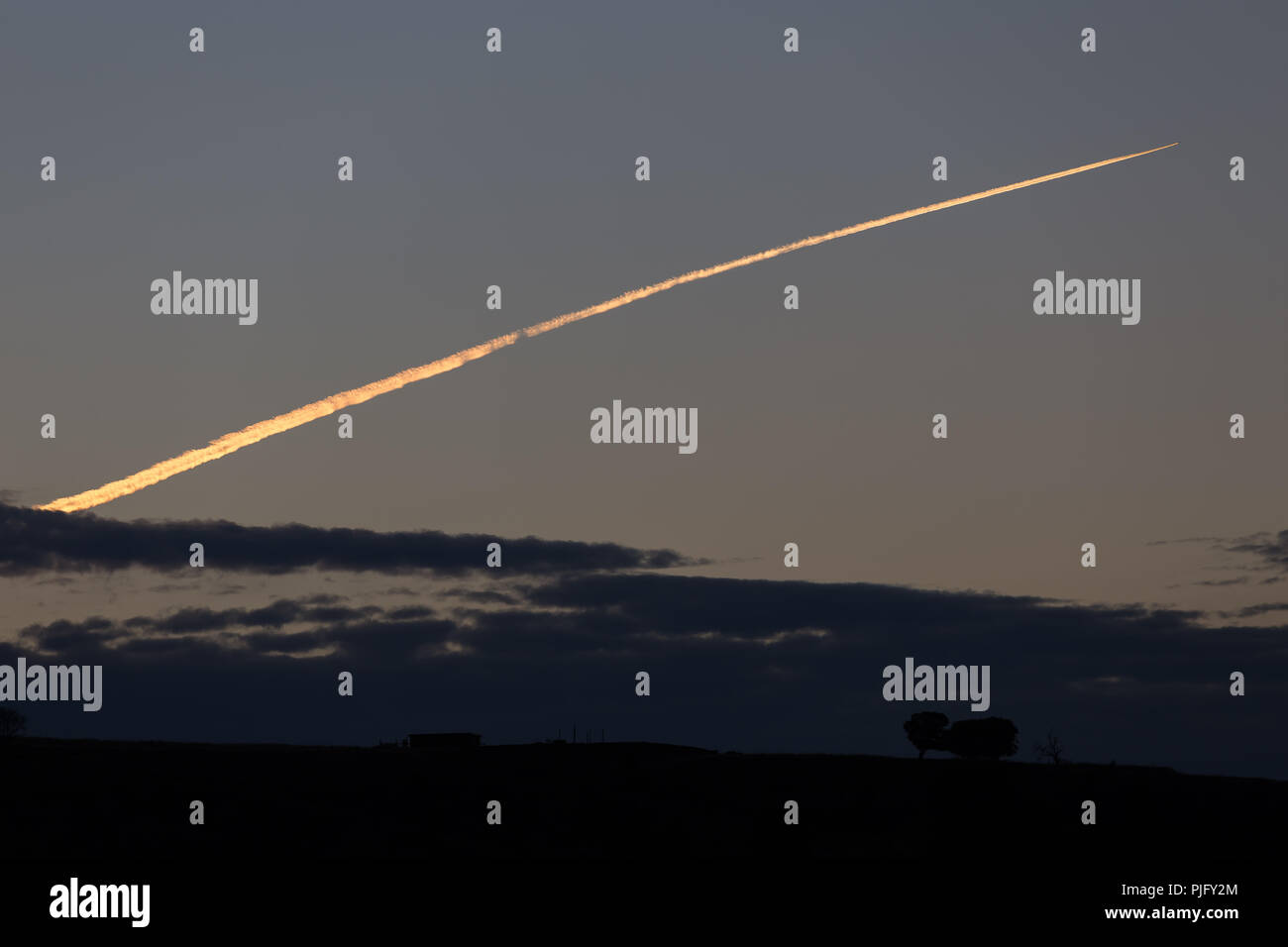 Traînée de condensation d'un avion tôt le matin par la lumière du soleil Banque D'Images