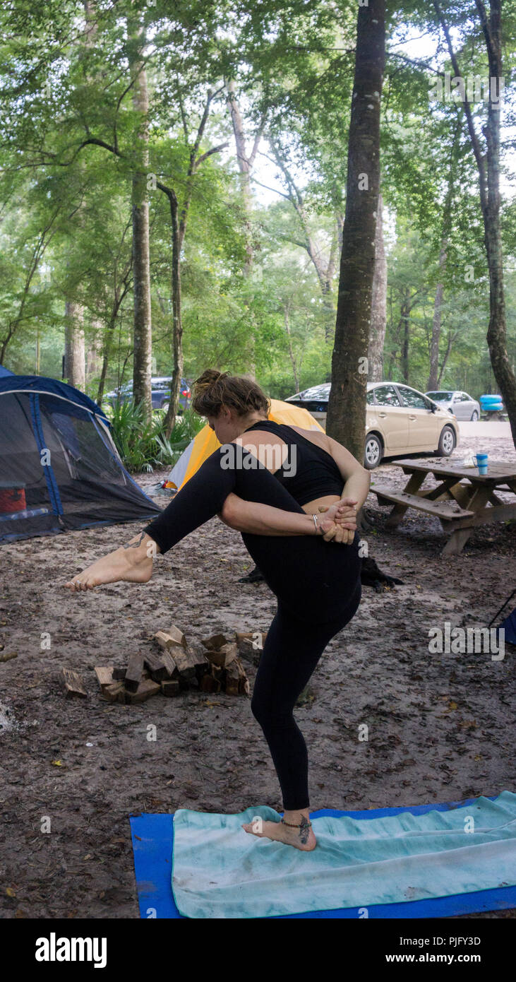 Jeune femme en Thiruvikramasana / Split permanent yoga pose tout en camping dans la forêt Banque D'Images