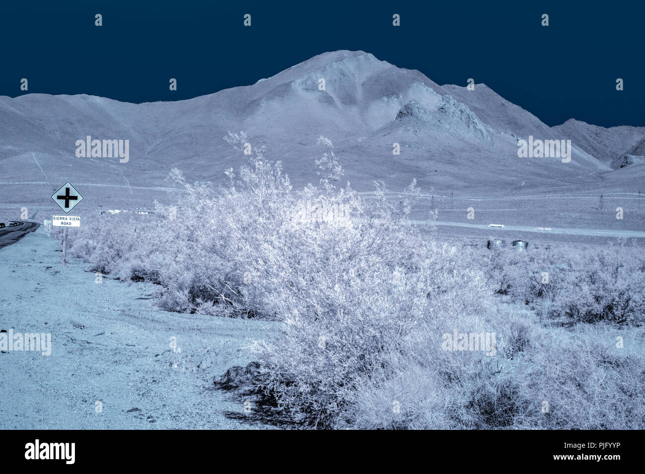 Vue de la route de buissons, blanc et plaque de rue des montagnes du désert aride sous un ciel bleu foncé. Banque D'Images