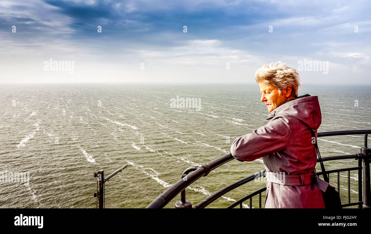 Senior Woman regardant le temps orageux het IJsselmeer du phare lors de l'historique village de pêcheurs d'Urk aux Pays-Bas Banque D'Images