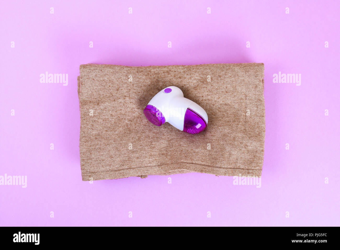 Une machine pour enlever les peluches dans la main. Pullover avec bobble sur un fond pastel violet Banque D'Images