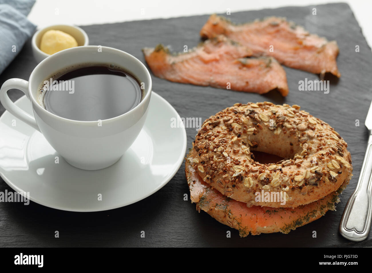 Sandwich bagel au saumon et une tasse de café sur une planche à découper ardoise Banque D'Images