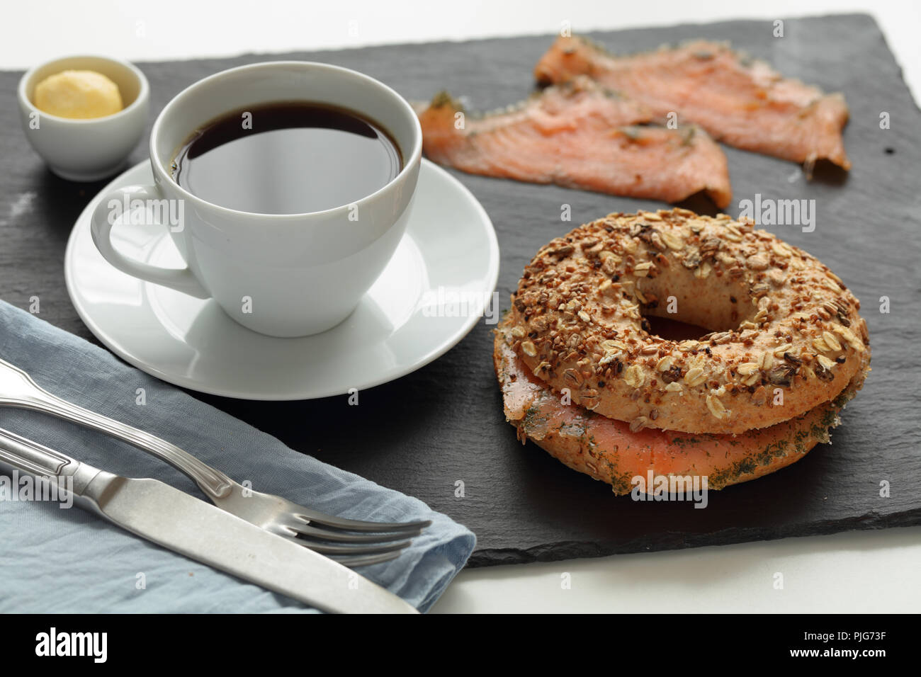 Sandwich bagel au saumon et une tasse de café sur une planche à découper ardoise Banque D'Images