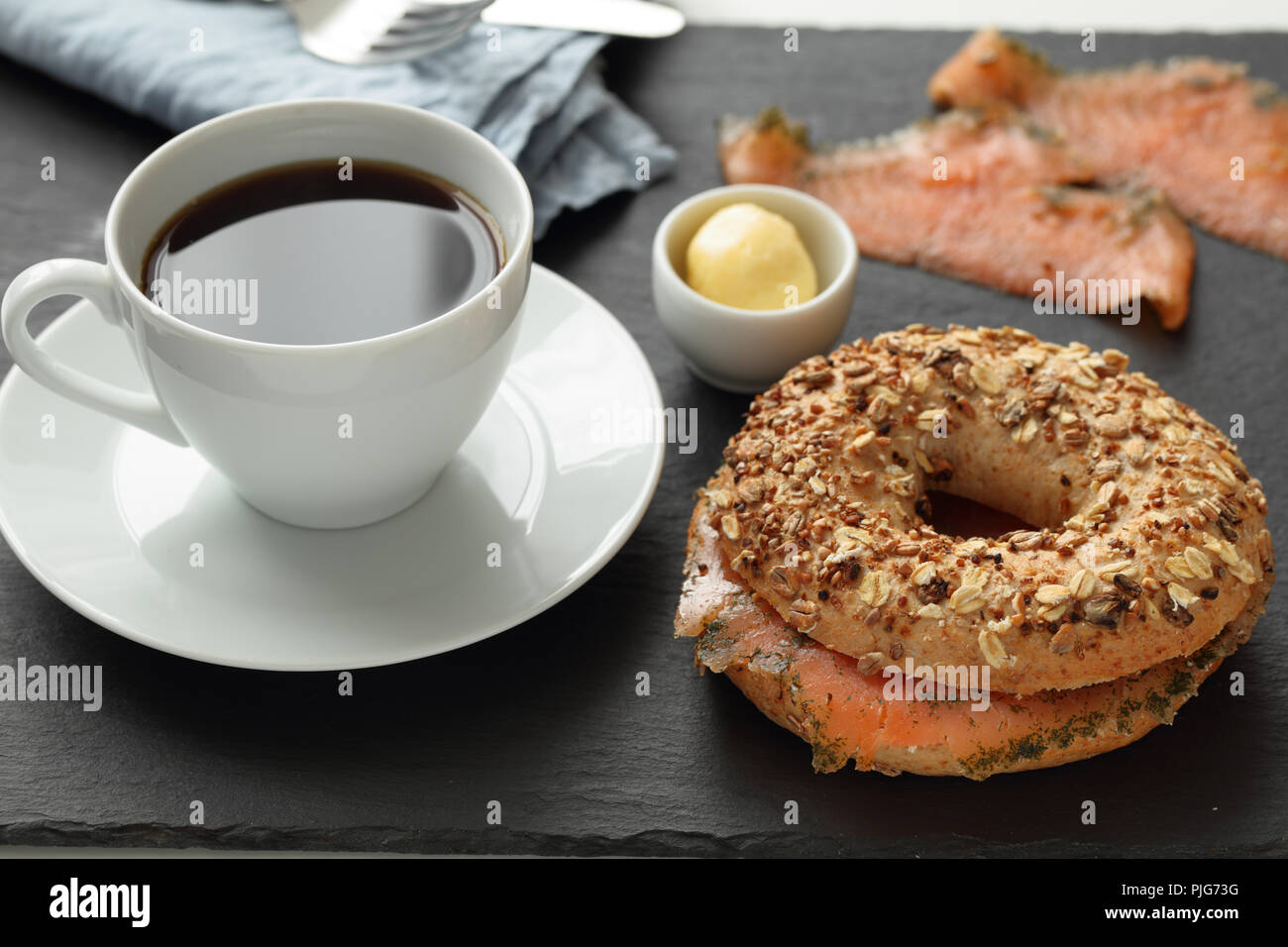 Sandwich bagel au saumon et une tasse de café sur une planche à découper ardoise Banque D'Images