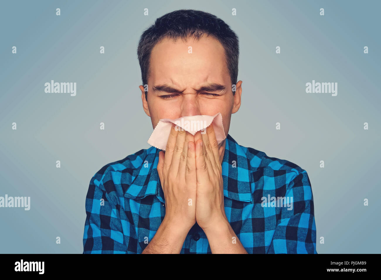 Homme malade a isolé l'écoulement nasal. Un jeune mec éternue dans une écharpe rose sur un fond bleu. Les rhumes de l'automne. Banque D'Images