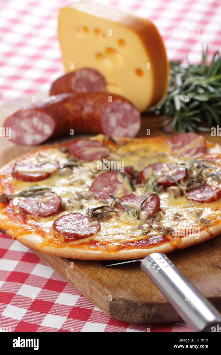 Pizza à la saucisse, le boeuf haché, le fromage et le romarin sur la planche à découper en bois Banque D'Images