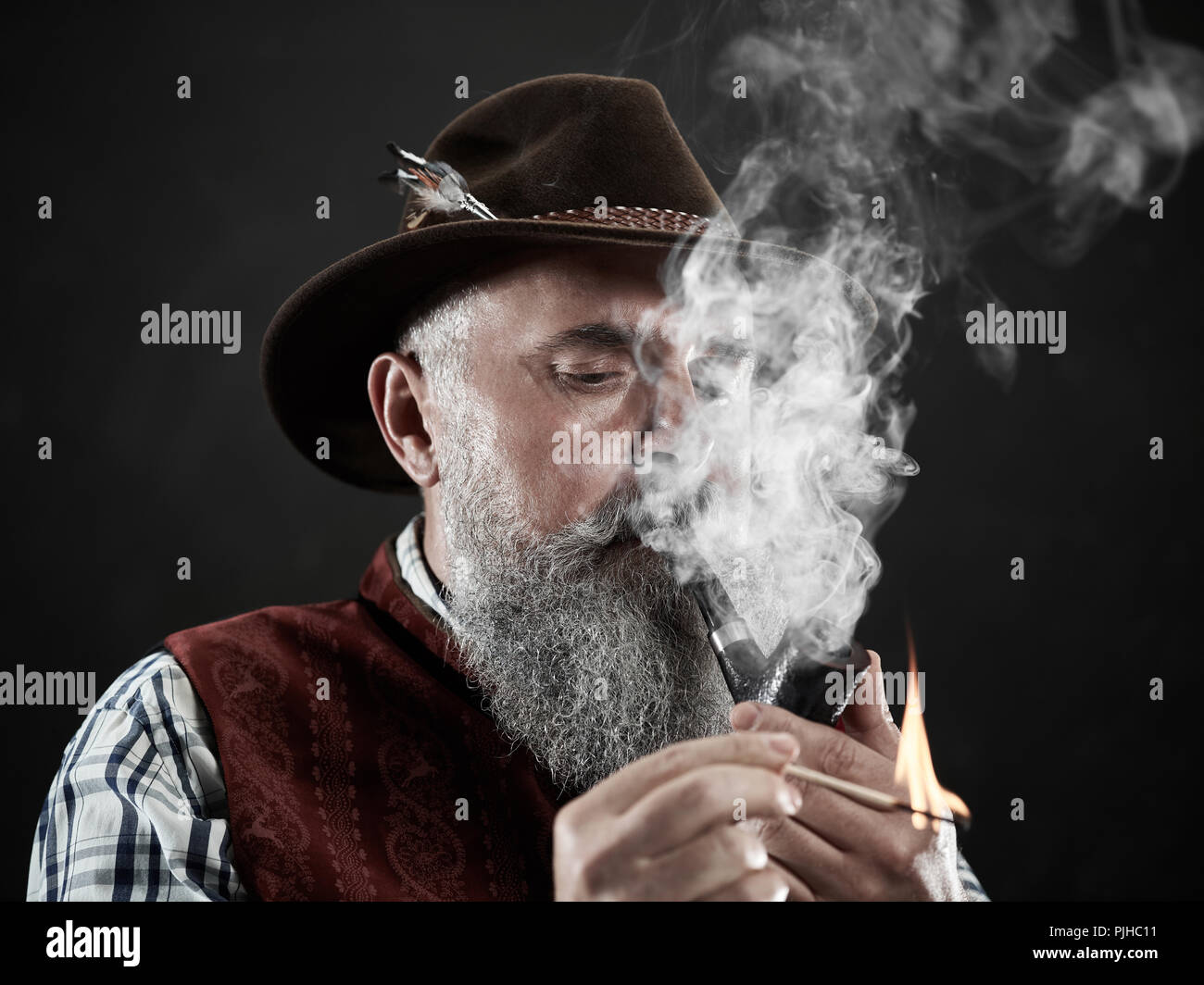 Dramatique en noir et blanc portrait of senior man in hat fumer le tabac pipe. Vue de profil d'Austrian, tyrolienne, vieil homme Bavarois Banque D'Images