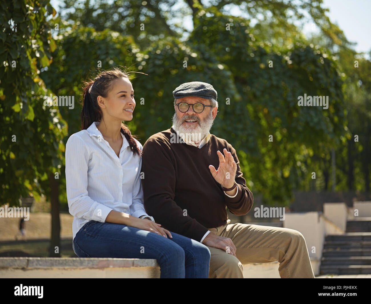 Aider quelqu'un que vous aimez. Portrait of young smiling girl embracing grand-père contre city park. communauté et de vie de la famille concept Banque D'Images