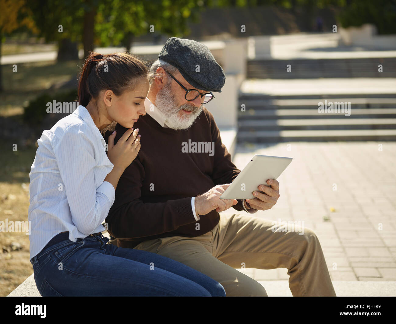 Aider quelqu'un que vous aimez. Portrait of young smiling girl sitting avec grand-père et l'ordinateur portable contre city park. communauté et de vie de la famille concept Banque D'Images