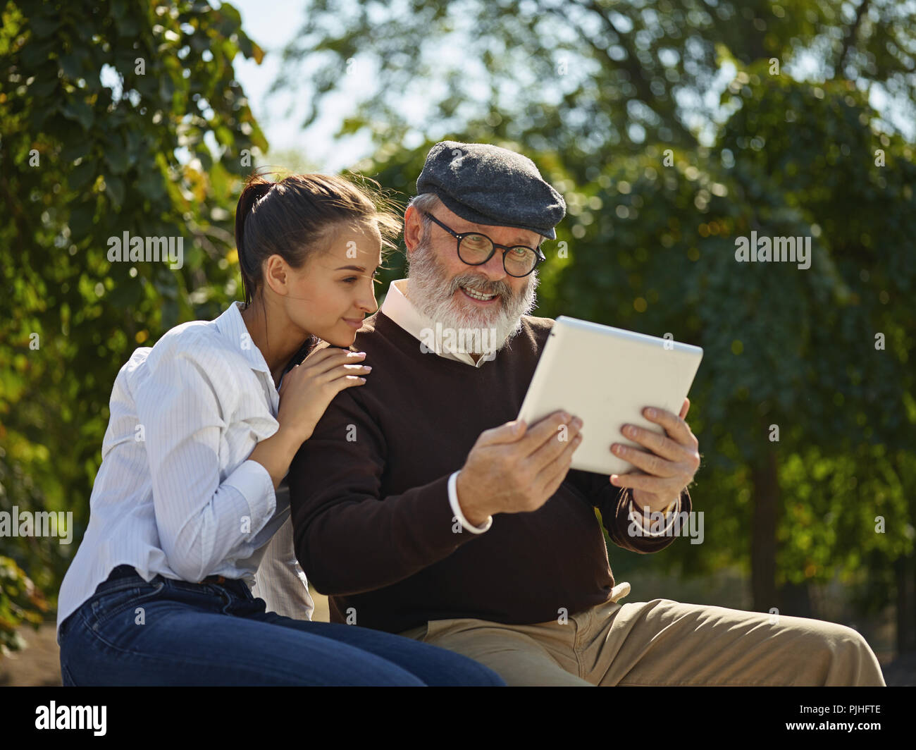 Aider quelqu'un que vous aimez. Portrait of young smiling girl sitting avec grand-père et l'ordinateur portable contre city park. communauté et de vie de la famille concept Banque D'Images