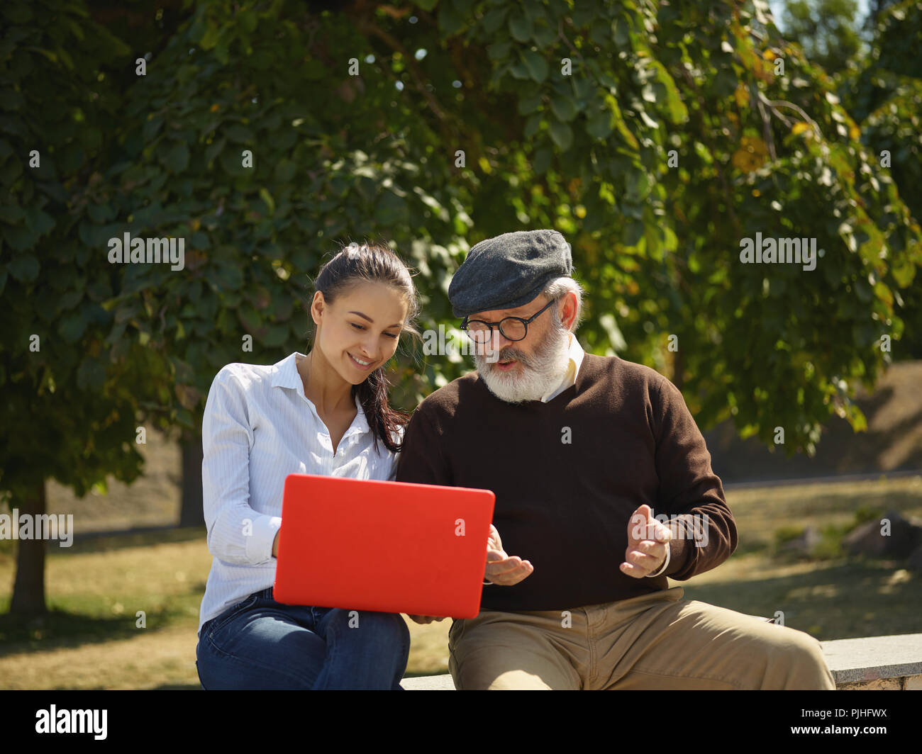 Aider quelqu'un que vous aimez. Portrait of young smiling girl sitting avec grand-père et l'ordinateur portable contre city park. communauté et de vie de la famille concept Banque D'Images