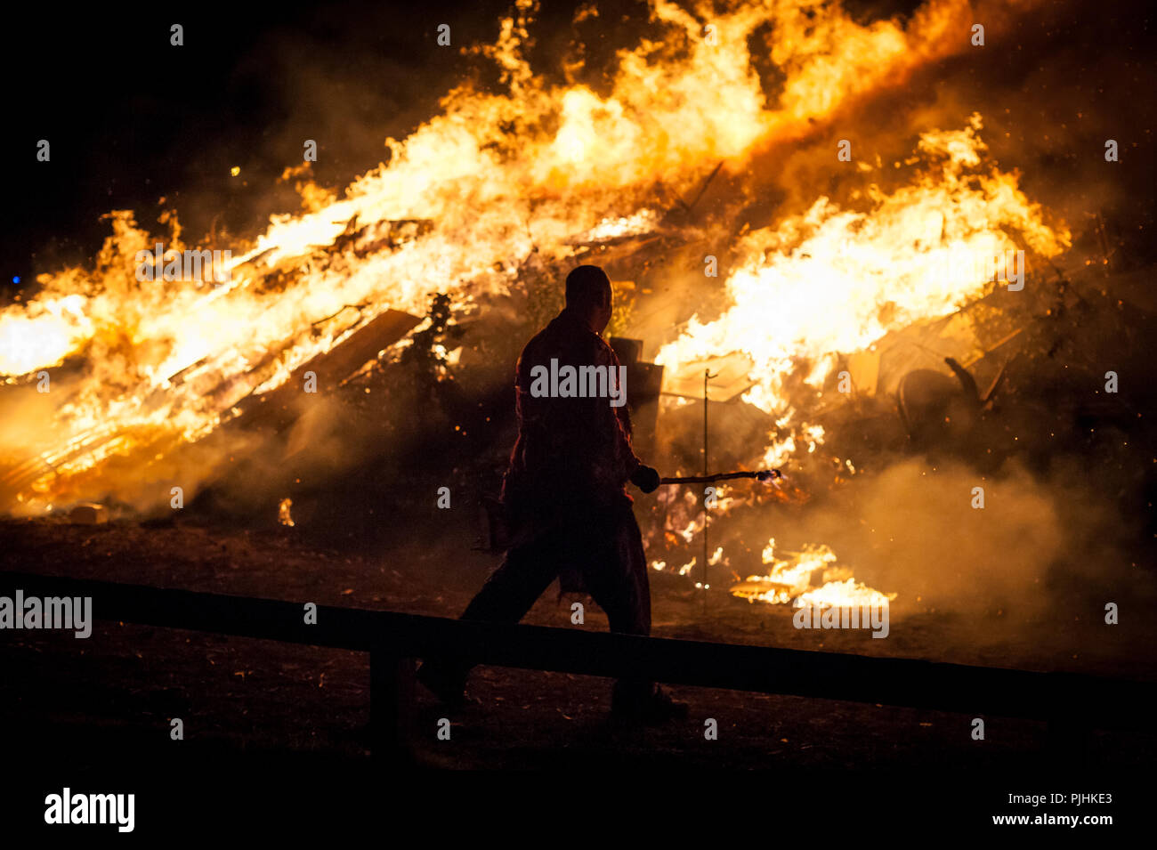 Un homme marche devant un feu brûlant d'un feu de camp pendant la nuit à l'occasion des célébrations du 5e novembre à Littlehampton, West Sussex, UK. Banque D'Images