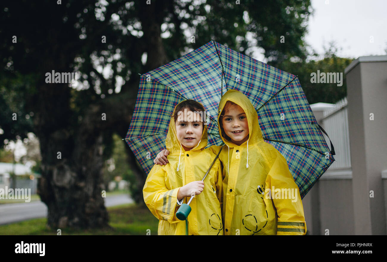 Portrait de deux belles filles debout sous un parapluie. Deux sœurs portant des vêtements imperméables à l'extérieur debout parapluie un jour de pluie. Banque D'Images