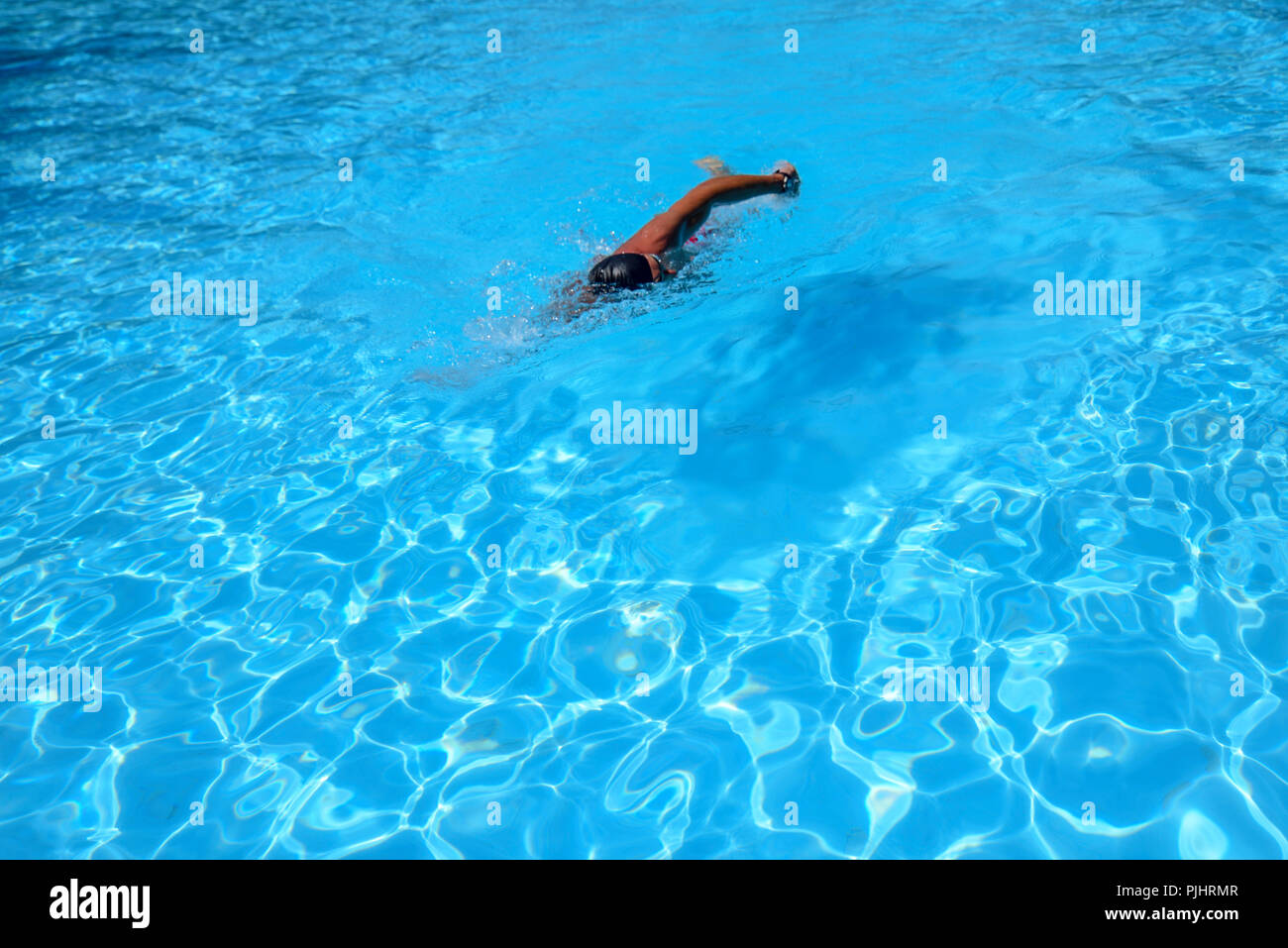 Man en nage libre dans une piscine extérieure sur une journée ensoleillée. L'homme porte un maillot rouge et un capuchon noir. fit man natation pendant les loisirs Banque D'Images