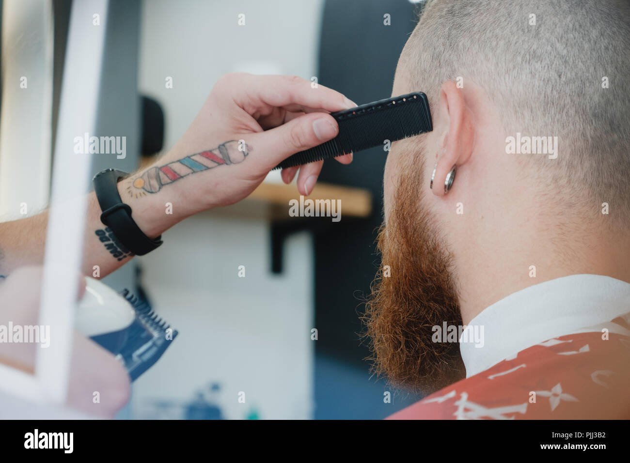 Un beau jeune homme barbu dans un salon de coiffure. Le salon de coiffure  brosses ses cheveux et coupe avec une tondeuse électrique Photo Stock -  Alamy