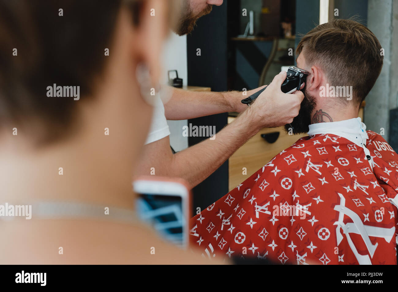 Un beau jeune homme barbu dans un salon de coiffure. Le salon de coiffure brosses ses cheveux et coupe avec une tondeuse électrique. Banque D'Images