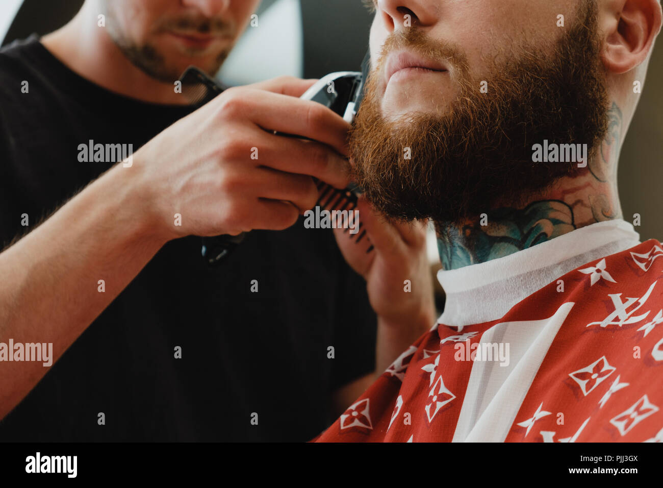 Un beau jeune homme barbu dans un salon de coiffure. Le salon de coiffure brosses ses cheveux et coupe avec une tondeuse électrique. Banque D'Images