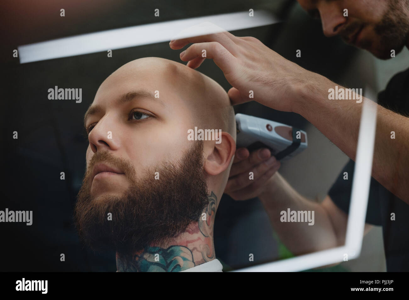 Un bel homme barbu dans un skinhead barbershop. Le barbier se rase la tête avec une tondeuse électrique. Banque D'Images