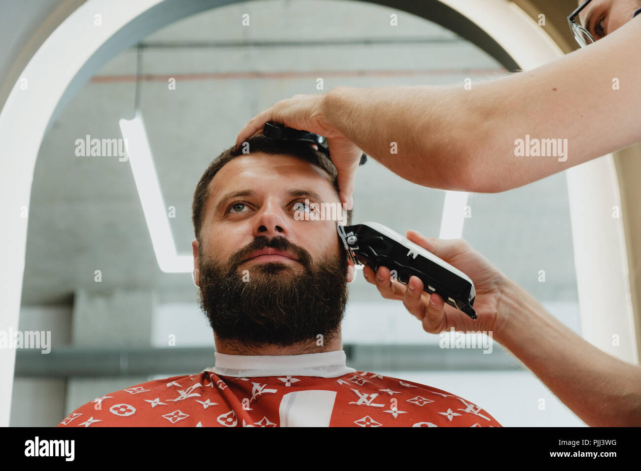 Un bel homme barbu dans un salon de coiffure. Le salon de coiffure brosses ses cheveux et coupe avec une tondeuse électrique. Banque D'Images