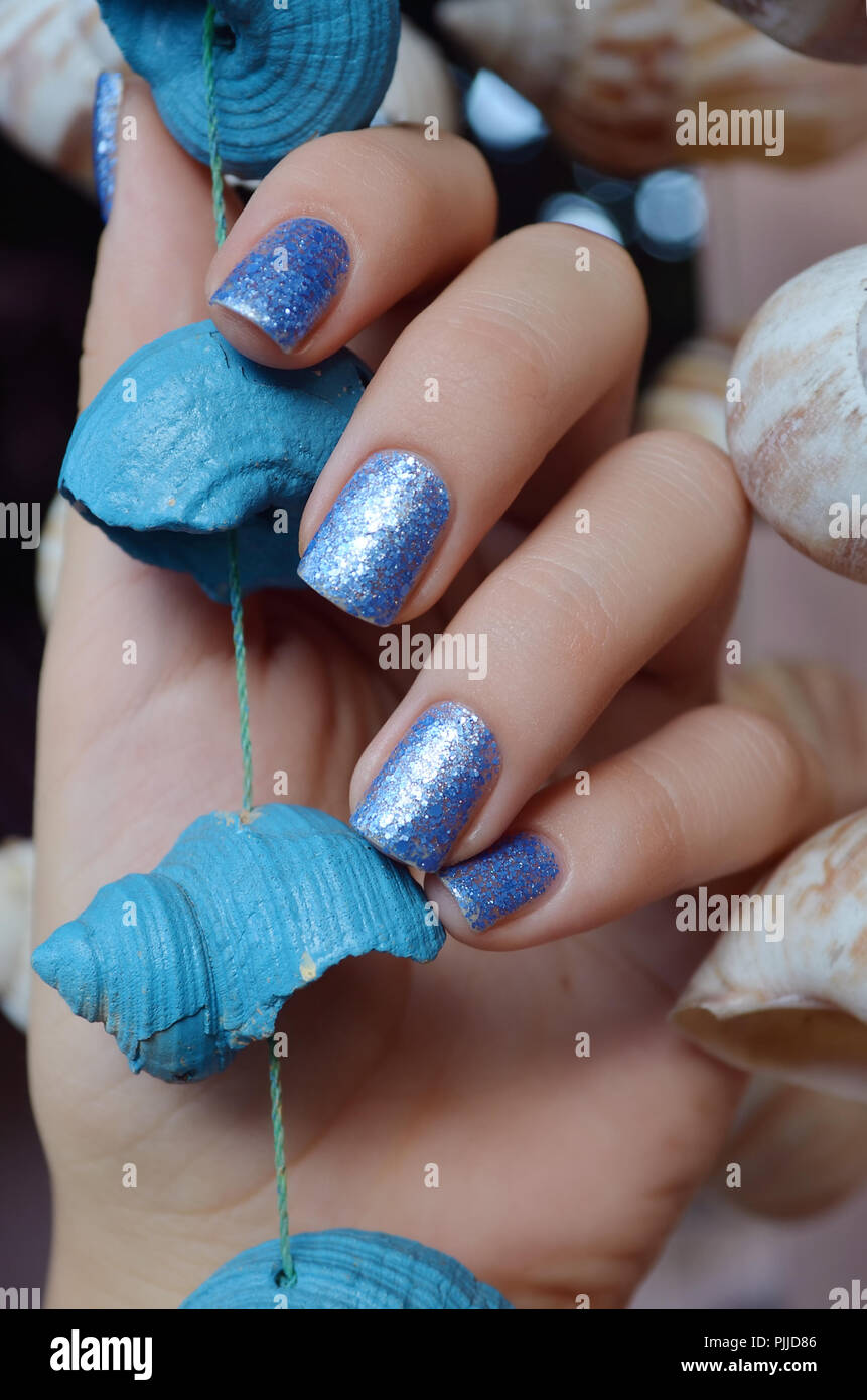 Femmes avec blue glitter nail design holding sea shell. Banque D'Images