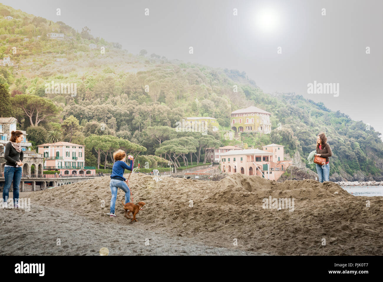 Italie LEVANTE - le 24 avril 2011 ; la lumière vive derrière littoral méditerranéen beach village situé en dessous de colline avec avec trois femmes en vacances sur dunes takin Banque D'Images