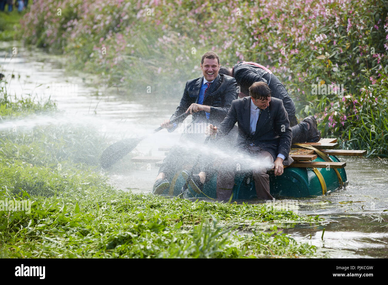 Trois portant costumes noirs se mettre à l'eau d'un tuyau flexible sur un radeau dans une rivière à la Plaine des jeux, Thorney, Somerset, Angleterre Banque D'Images